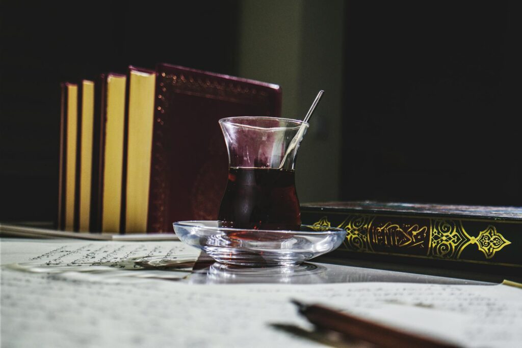 Does Black Tea Help in Weight Loss? A glass of black tea on a table with ornate books including the Quran, enhancing a scholarly atmosphere. Does Black Tea Help in Weight Loss?