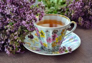 A beautiful porcelain teacup with floral patterns, filled with herbal tea, surrounded by lavender flowers.